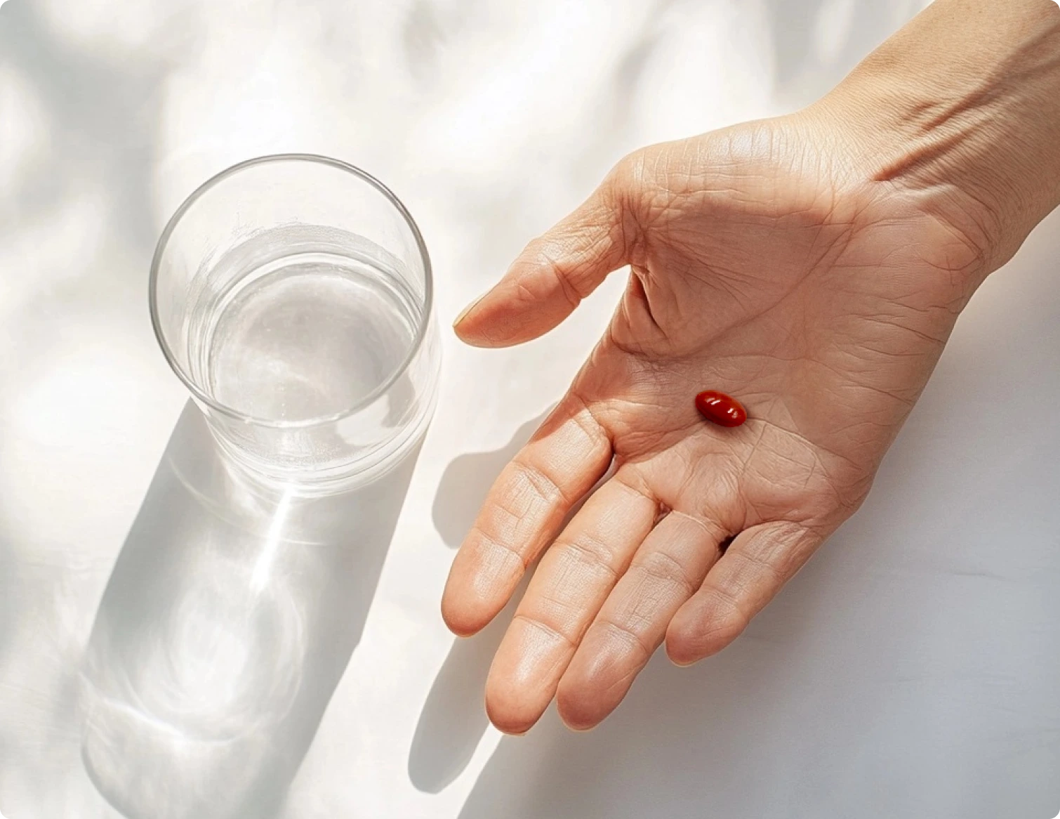 A PreserVision AREDS 2 minigel in the palm of a hand next to a glass of water