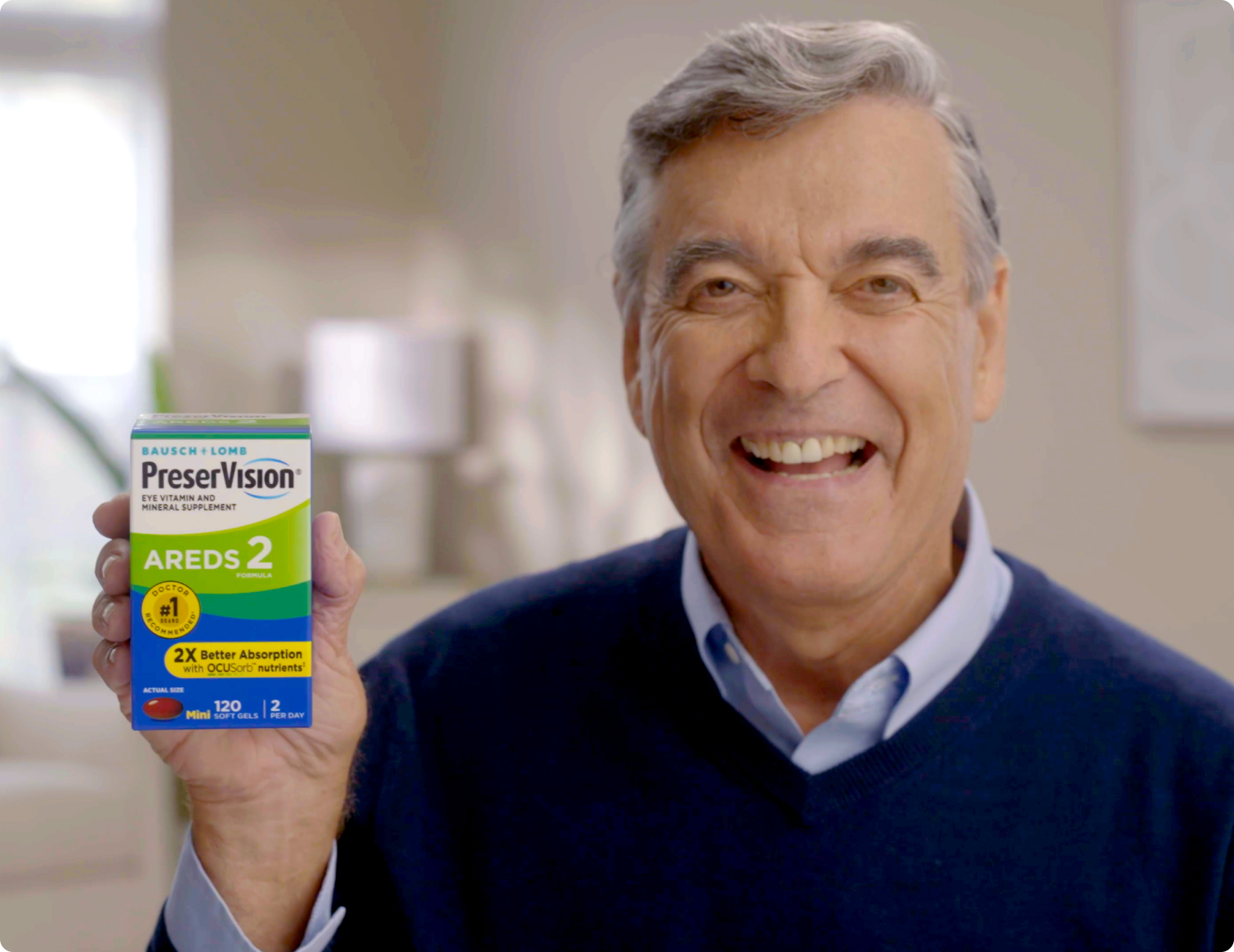 A man in his 60s smiling and holding up a package of PreserVision AREDS 2 Eye Vitamins.